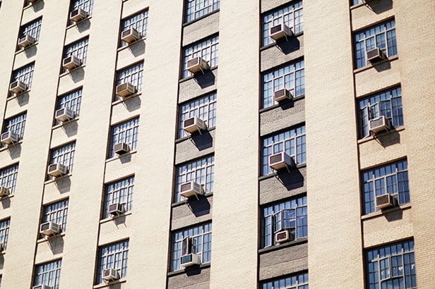 tan apartment building with air conditioning units coming out of most windows
